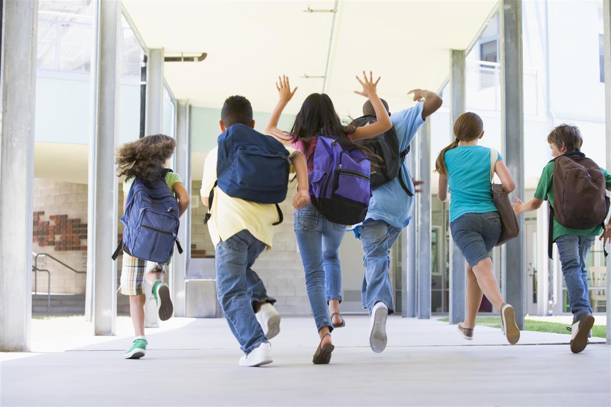 Barn med skolesekker på ryggen som løper bortover en korridor bortover en  - Klikk for stort bilde